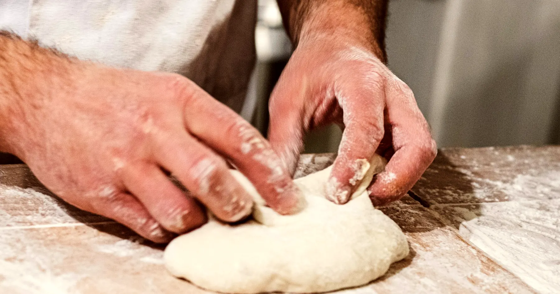 Mains qui façonnent la pâte sur le plan de travail fariné